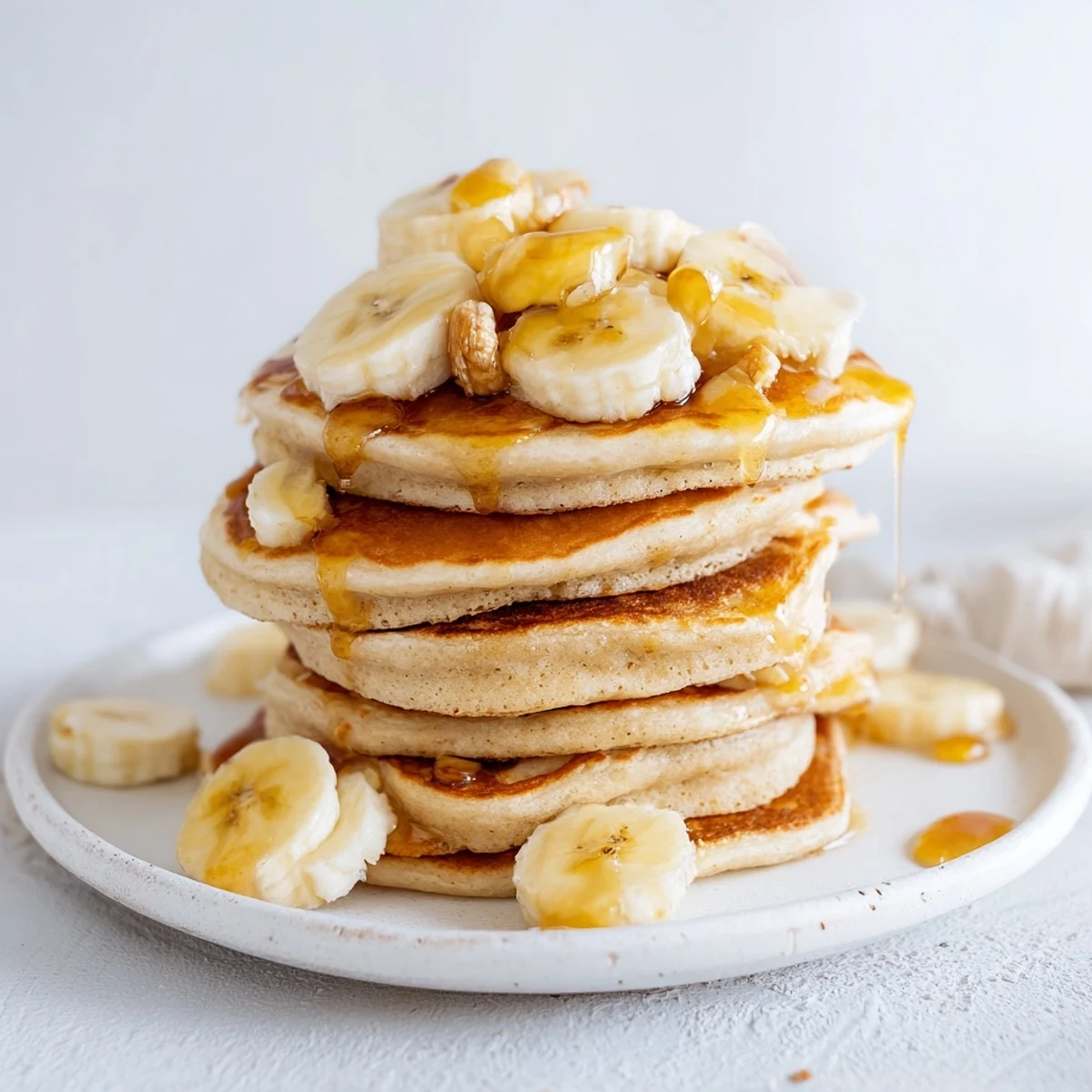 Golden-brunch banana pancakes, stacked high, drizzled with warm maple syrup, perfect for a cozy weekend.