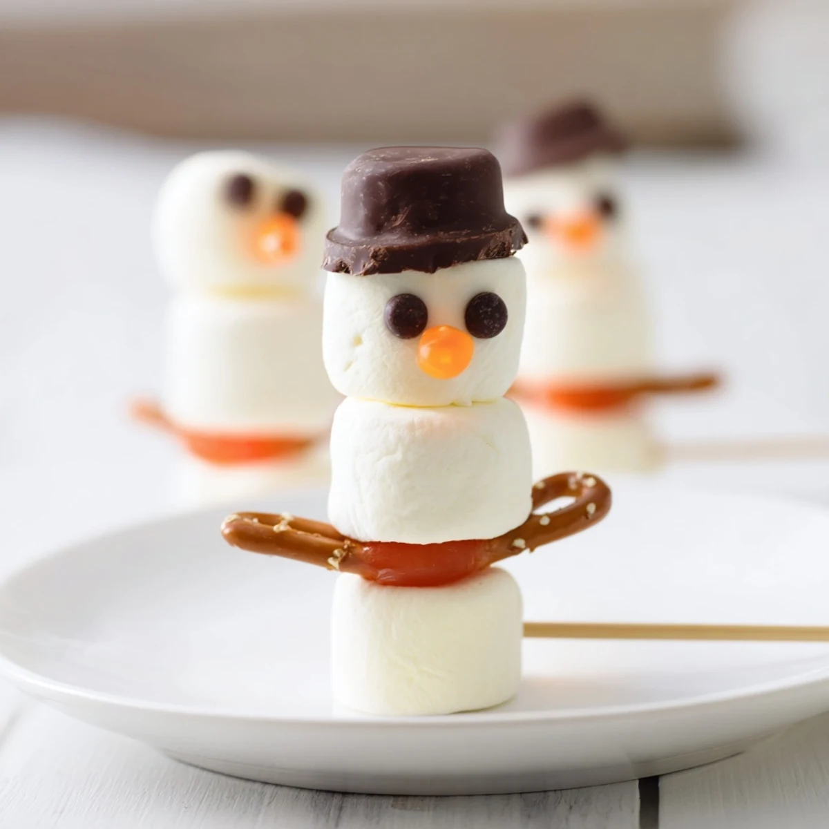 Homemade marshmallow snowman stick treats, complete with candy scarves and hats, a festive winter dessert.