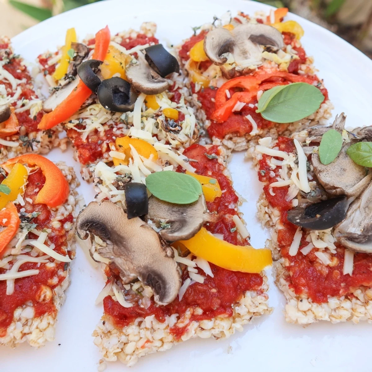 Crispy rice cake pizza squares, baked with melted cheese, fresh herbs, and colorful veggie toppings.