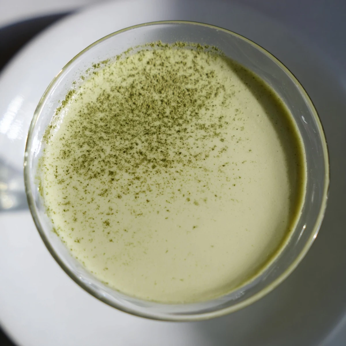 A frothy, vibrant Matcha Martini cocktail in a chilled glass, topped with a delicate dusting of green tea powder for a sweet, creamy sip.  