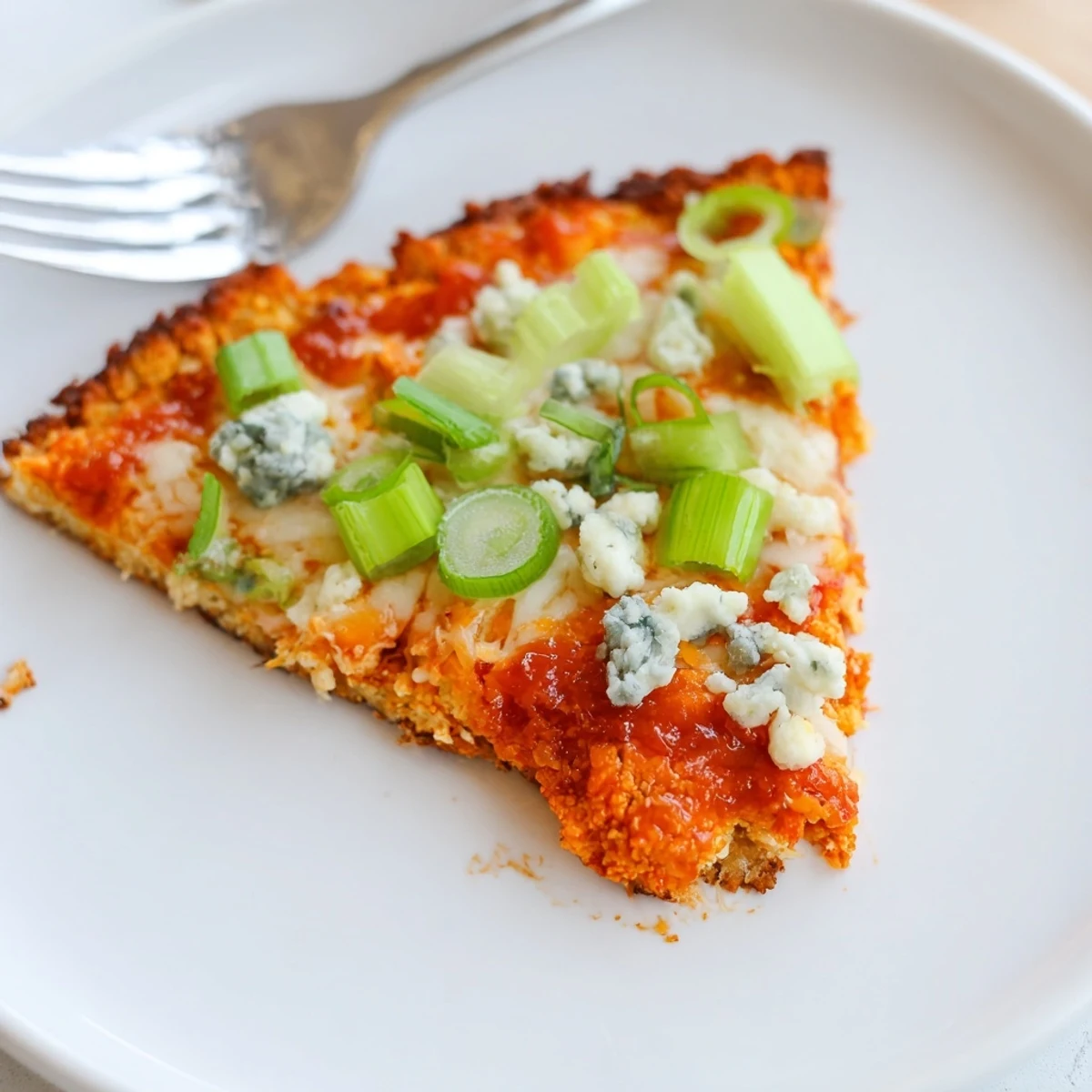 A close-up of a freshly baked Buffalo Cauliflower Pizza with golden crust, melted mozzarella, and vibrant green onion garnish on a wooden board.  