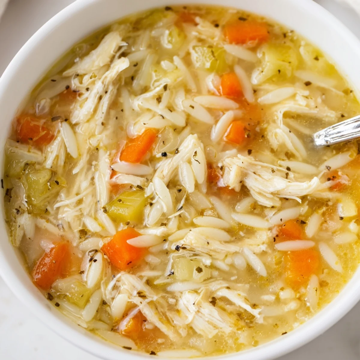 A comforting bowl of Lemon Pepper Chicken Orzo Soup, featuring tender shredded chicken and al dente pasta in a bright, steaming broth with lemon wedges on the side.  
