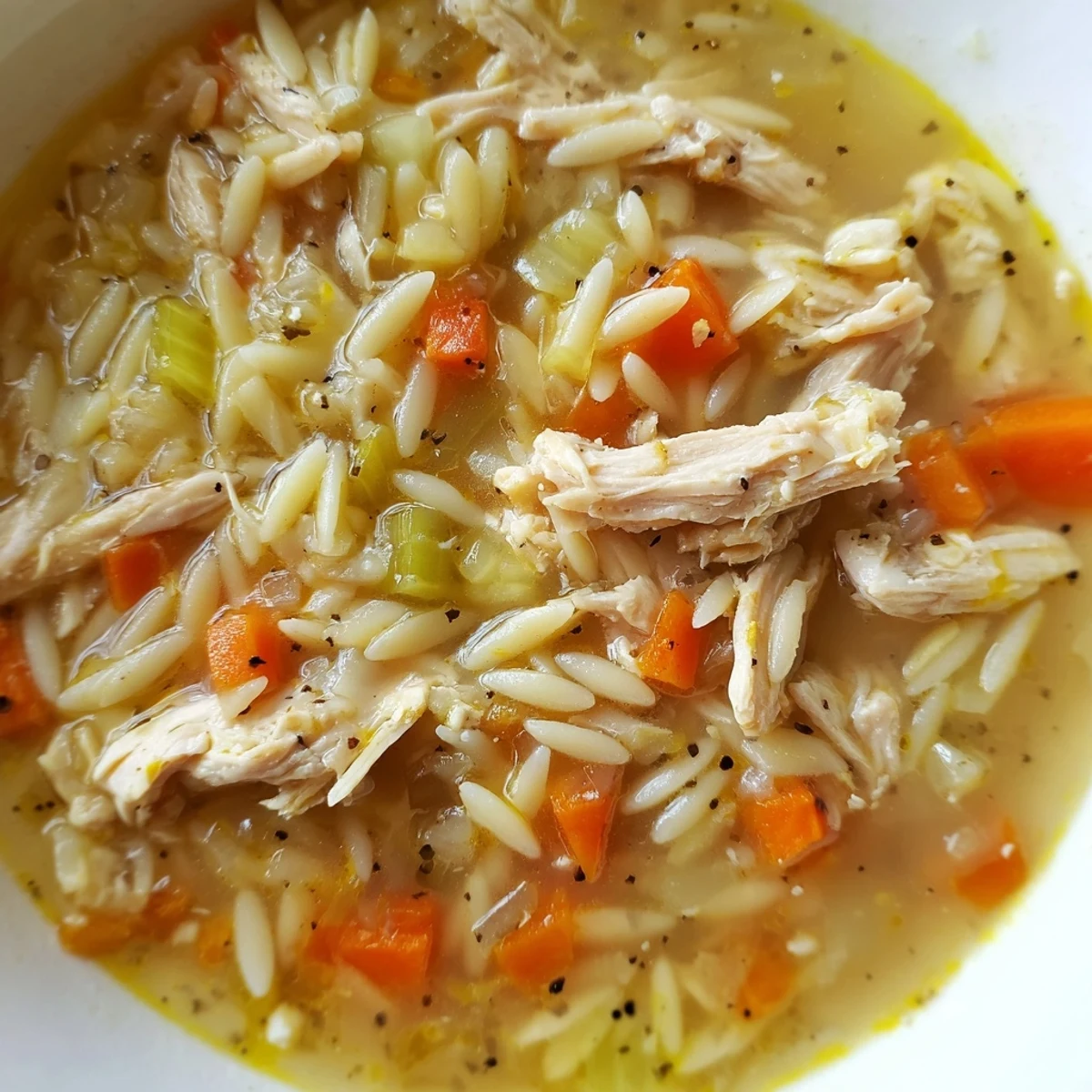 Hearty Lemon Pepper Chicken Orzo Soup in a white ceramic bowl, with vibrant carrots and celery visible in the golden, aromatic broth.