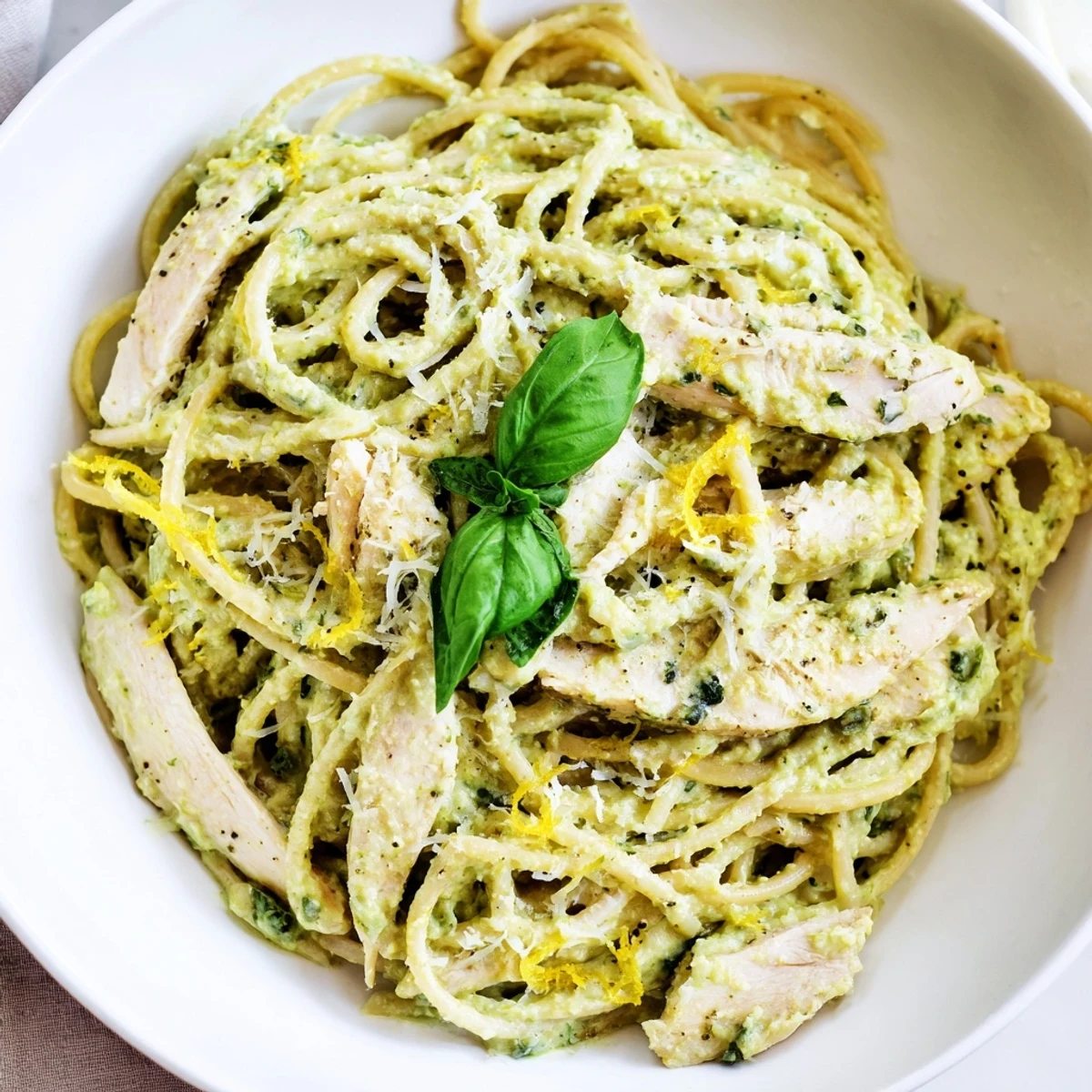 Creamy Avocado Chicken Pasta featuring al dente spaghetti tossed in a vibrant green avocado sauce, garnished with fresh basil and lemon zest.  