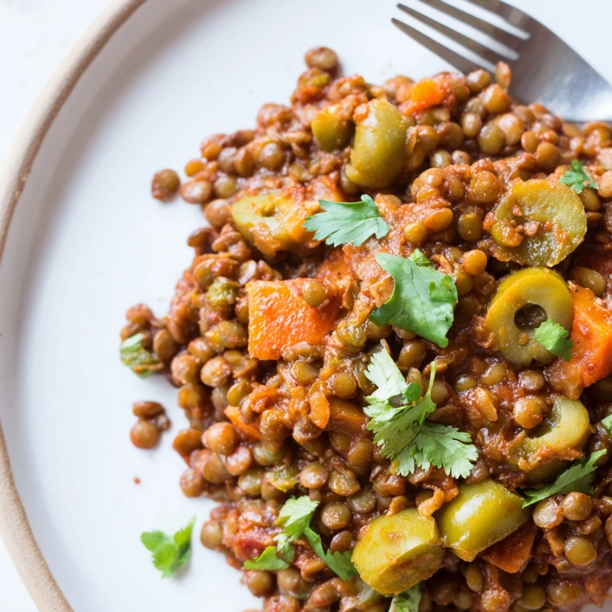 A close-up of plant-based Cuban-Inspired Lentil Picadillo reveals a hearty skillet of spiced lentils, chopped carrots, and bell peppers simmering with tomato paste and savory seasonings.