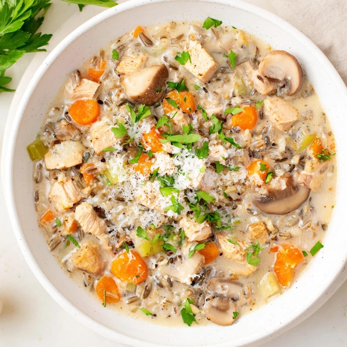 A comforting bowl of creamy Parmesan Mushroom Chicken and Wild Rice Soup garnished with fresh parsley.