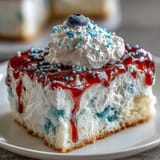 Colorful Memorial Day poke cake with red and blue gelatin swirls in white cake, topped with fluffy whipped topping and patriotic sprinkles.