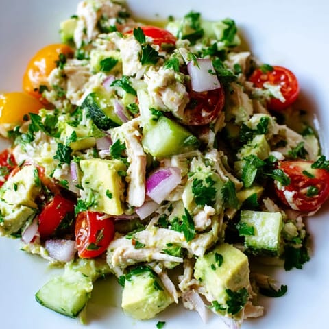 A close-up of chilled Avocado Chicken Salad tossed with red onion, cucumber, and fresh cilantro on a marble countertop.  
