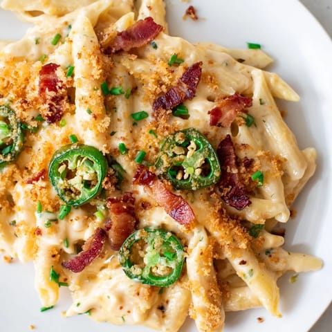 A skillet of golden, bubbling Jalapeño Popper Pasta topped with crunchy panko crumbs and fresh chives on a rustic table.  