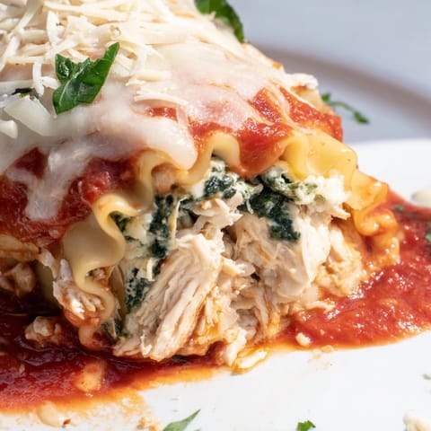Rustic Italian-American Chicken and Spinach Lasagna Rolls on a baking dish, oozing ricotta and spinach filling beside fresh bread.  