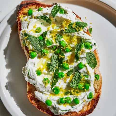 Vibrant green pea and mint ricotta spread on crunchy toast, served with lemon wedges for a zesty brunch.
