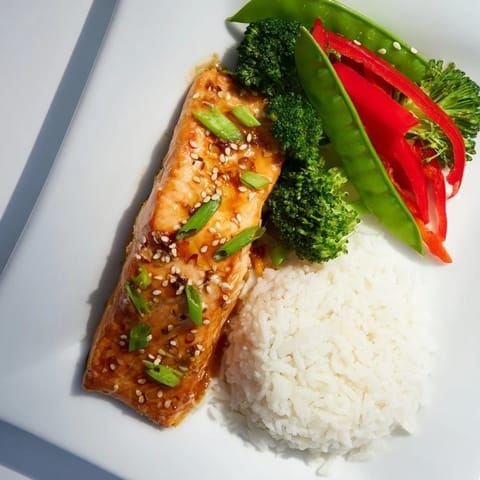 Perfectly glazed salmon over steamed jasmine rice and crisp snap peas, garnished with green onions and sesame seeds.