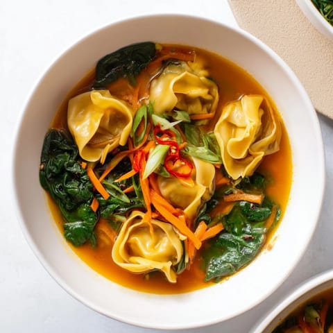 Hearty Red Curry Wonton Soup with Greens served in a rustic bowl, showcasing colorful carrots and bok choy floating in a creamy, aromatic Thai-inspired broth.