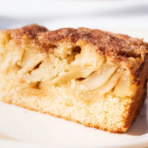 A slice of Baked Apple Cake, topped with powdered sugar, on a cozy brunch table.