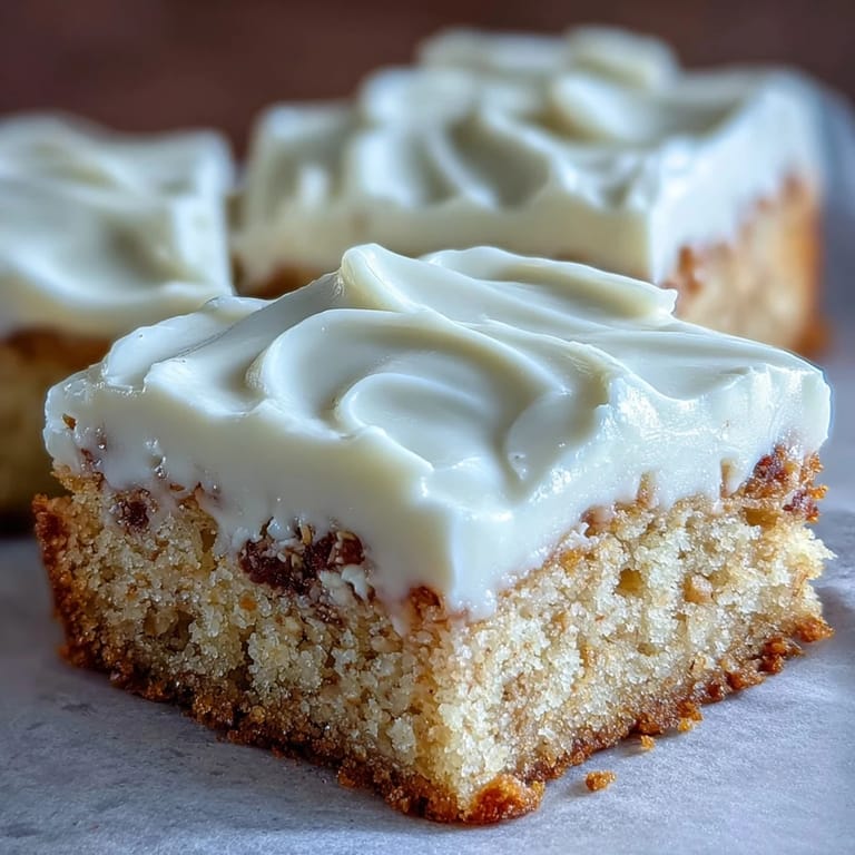 Freshly baked almond flour sugar cookie bars stacked high, featuring a creamy topping and tender crumb texture.