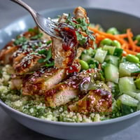 Freshly baked, tender chicken slices rest on Mediterranean pearl couscous in a vibrant Sesame Ginger Chicken Couscous Bowl, garnished with crunchy veggies and herbs.