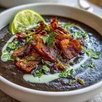 A rich, creamy black bean soup topped with crispy bacon and zesty lime crema for a satisfying, hearty meal.  