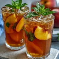 Refreshing iced peach green tea lemonade in a clear glass with ice, garnished with peach slices and mint leaves.  